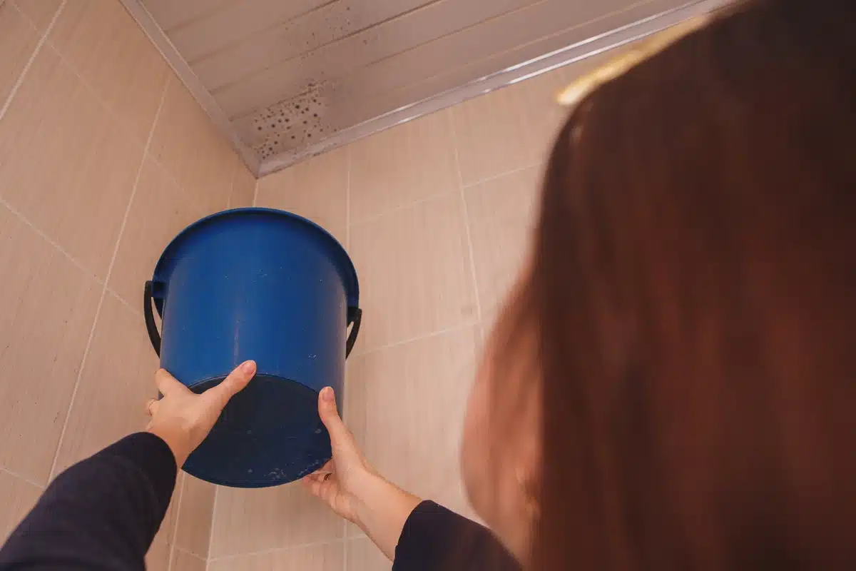 woman holding bucket to stop water dripping from the ceiling
