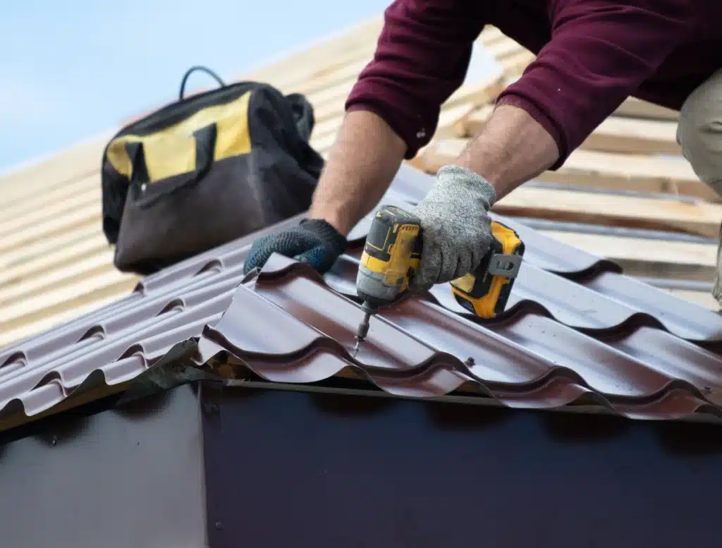professional roofer using drill to install red metal roof tile on wood structure