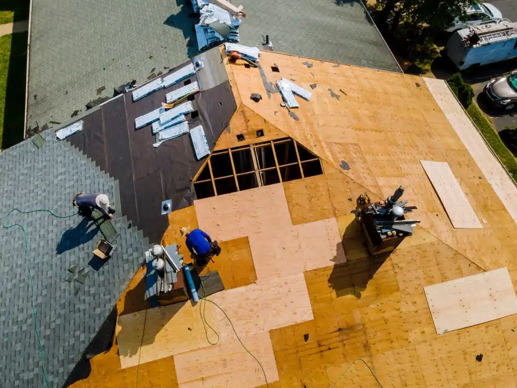 Two roofers are replacing the roof deck and asphalt shingles on a house