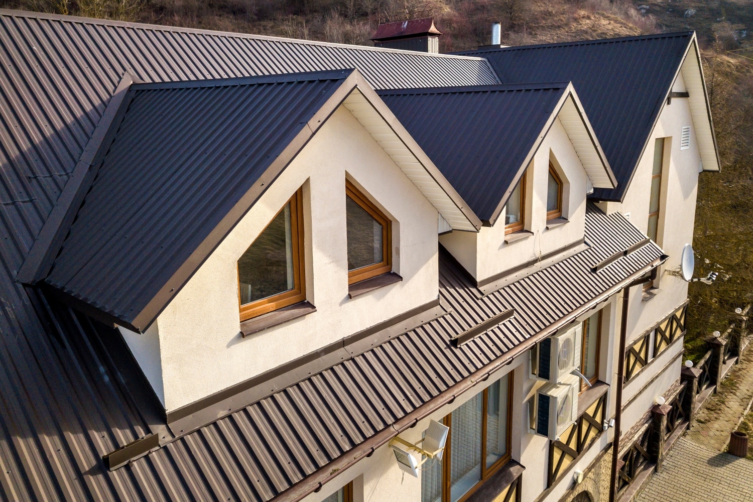 Side aerial view of a house with a metal roof and underlayment, showing construction or roofing work in progress