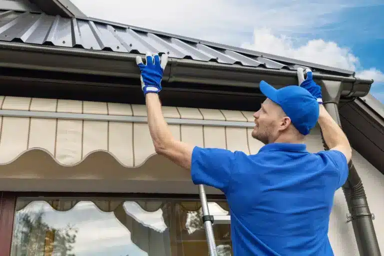 metal roof installation-roof tech in blue standing on a ladder installing metal roofing materials