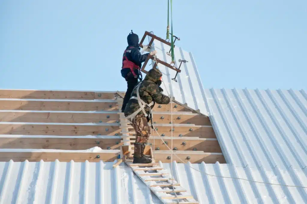metal roof installation-two roof techs standing on rafters installing metal roof panels