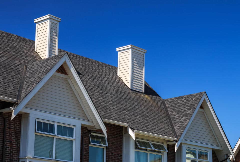 affordable roofing-dark gray shingled roof on a home with cream siding and brick