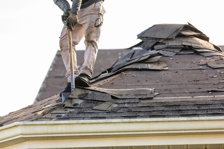 roof tear off-roof tech standing on a roof using a shovel to remove old shingles