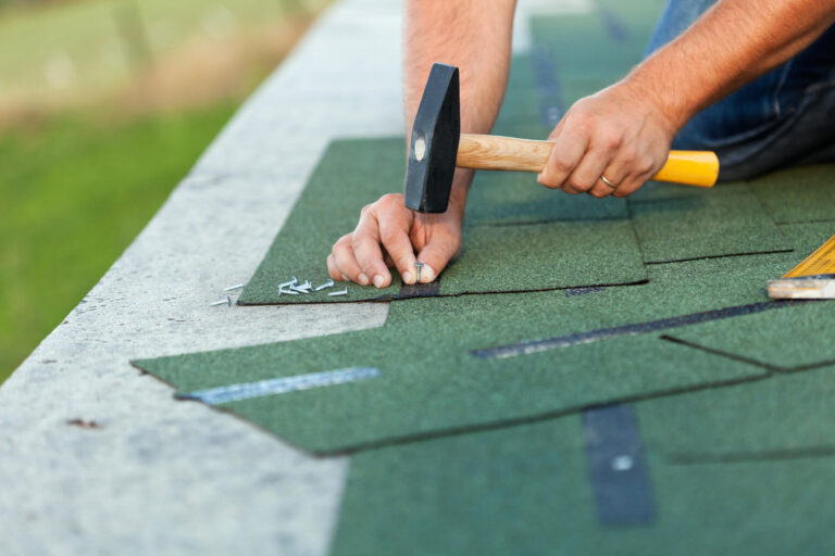 where to nail shingles-close up of a man using a hammer to nail green shingles to a roof