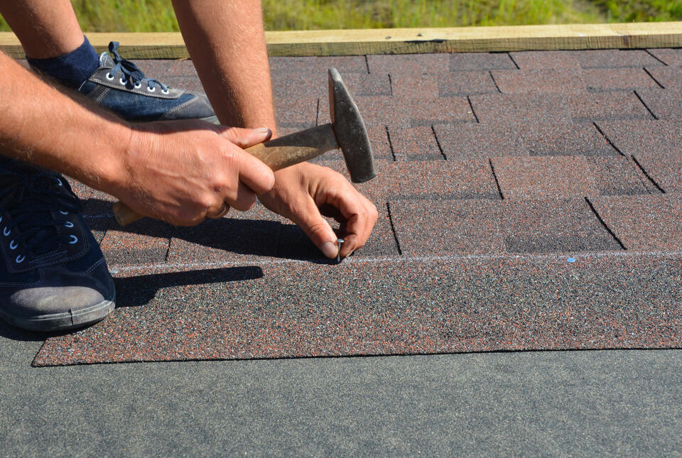 where to nail shingles-man using a hammer to manually install brown shingles on a roof