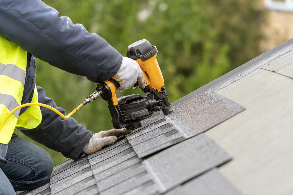 where to nail shingles-roof tech in a safety vest using powertools to install gray shingles on a roof