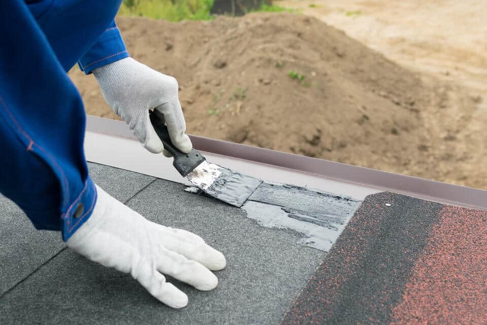roof sealant-man wearing protective gloves applying sealant under roof shingles