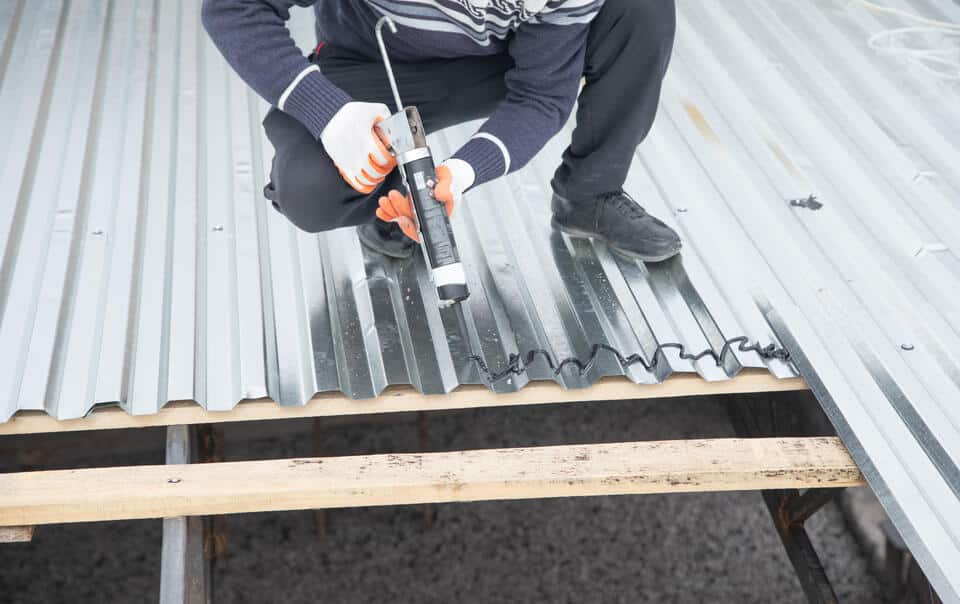 roof sealant-overhead view of a man wearing protective gloves applying sealant to corrugated metal roofing