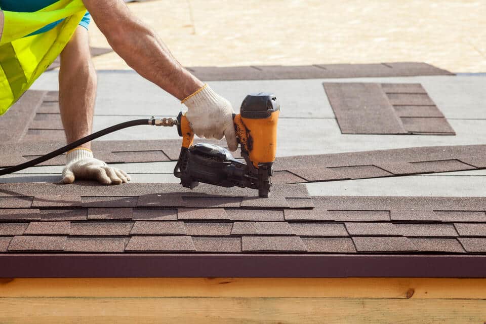 roofing tools-roofer wearing safety gear using a power tool to install shingles on roof