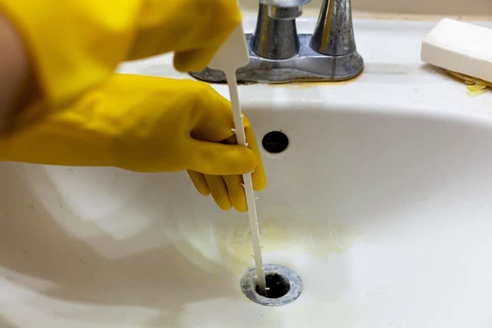unclog bathroom sink-gloved hand using snake to clear bathroom sink